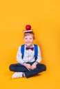 Excited cute schoolboy with book and red apple on head sitting on yellow background Royalty Free Stock Photo