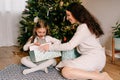 Excited daughter and mother sitting at home near beautiful decorated Christmas tree and enjoying opening their presents Royalty Free Stock Photo
