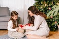 Excited daughter and mother sitting at home near beautiful decorated Christmas tree and enjoying opening their presents Royalty Free Stock Photo