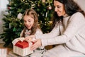 Excited daughter and mother sitting at home near beautiful decorated Christmas tree and enjoying opening their presents Royalty Free Stock Photo