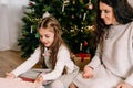 Excited daughter and mother sitting at home near beautiful decorated Christmas tree and enjoying opening their presents Royalty Free Stock Photo