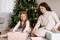 Excited daughter and mother sitting at home near beautiful decorated Christmas tree and enjoying opening their presents Royalty Free Stock Photo