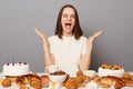 Excited delighted woman wearing white T-shirt rejoicing delicious various desserts, isolated over gray background screaming with Royalty Free Stock Photo