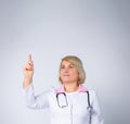 Excited doctor, blonde woman isolated on gray background. Female doctor in white medical gown point index finger up. Healthcare, Royalty Free Stock Photo