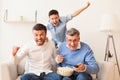 Excited Elderly Man, Mature Son And Grandson Watching Sports Indoor