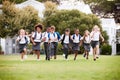 Excited Elementary School Pupils Wearing Uniform Running Across Field At Break Time Royalty Free Stock Photo