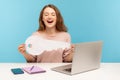 Excited emotions about house purchase. Amazing woman sitting at workplace with laptop, holding big paper key Royalty Free Stock Photo