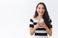 Excited, enthusiastic good-looking asian woman in casual outfit holding smartphone, thrilled smiling and looking camera