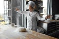 Excited enthusiastic young woman baker throwing flour on dough