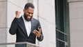 Excited ethnic bearded African American ethnicity millennial man entrepreneur businessman looking at mobile phone screen