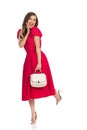 Excited Fashionable Woman In Red Dress, Gold High Heels And Beige Purse Is Standing On One Leg Royalty Free Stock Photo