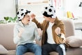 Excited father and teen son in football hats watching game and screaming on sofa at home, looking Royalty Free Stock Photo
