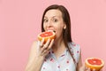 Excited funny young woman in summer clothes holding in hand, biting half of fresh ripe grapefruit isolated on pink Royalty Free Stock Photo