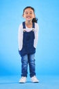 Excited girl child, fashion and studio portrait with jeans, dungaree and trendy style by blue background. Female kid