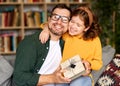 Excited girl daughter giving gift box for young loving father on holiday while sitting together on sofa Royalty Free Stock Photo
