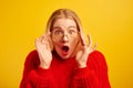 Excited girl dressed in red casual and glasses opened mouth in surprise and bulged eyes against yellow background, isolated. Portr Royalty Free Stock Photo