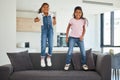 Excited girl kids jumping on living room sofa furniture at home for fun, energy and play games. Portrait crazy, happy