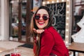 Excited girl with light-brown hair sending air kiss in cafe. Laughing gorgeous white woman in red jacket enjoying good