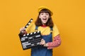 Excited girl teenager in french beret, denim sundress holding classic black film making clapperboard isolated on yellow Royalty Free Stock Photo