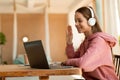 Excited girl teenager having video call with teacher from home, using laptop and wireless headset, waving at webcam Royalty Free Stock Photo