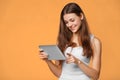 Excited girl in white shirt using tablet. Smiling woman with tablet pc, isolated on orange background