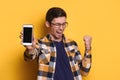 Excited glad young male posing with smartphone over yellow background