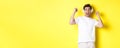 Excited handsome man dancing and singing along, listening music in headphones, standing over yellow background Royalty Free Stock Photo