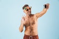 Excited happy adult man in swimwear posing isolated over blue wall background using mobile phone showing okay gesture take a