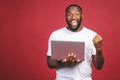 Excited happy afro american man looking at laptop computer screen and celebrating the win isolated over red background Royalty Free Stock Photo