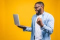 Excited happy afro american man looking at laptop computer screen and celebrating the win isolated over yellow background Royalty Free Stock Photo