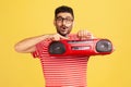 Excited happy bearded man in striped t-shirt and fashionable eyeglasses holding in hand red tape recorder, pushing play button Royalty Free Stock Photo