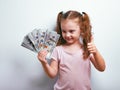 Excited happy kid girl holding money and thinking how to spend it showing thumb up sign by hand on blue background with empty copy Royalty Free Stock Photo