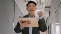 Excited happy mature businessman Asian man in office hallway with digital tablet win business success bet money lottery Royalty Free Stock Photo