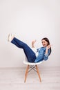 Excited happy pretty girl in casual jeans clothes raised hands and legs, sitting on white chair Royalty Free Stock Photo