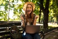 Excited happy woman outdoors sitting using laptop computer.