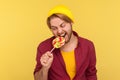 Excited hipster guy in beanie hat and checkered shirt biting lollipop candy, looking with crazy expression, craving