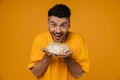 Excited hungry man in holding plate with cake isolated over yellow wall