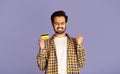 Excited Indian man with credit card gesturing YES on violet background