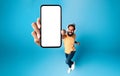 Excited indian man in headphones demontrating smartphone with blank screen while jumping up, mockup, above view Royalty Free Stock Photo