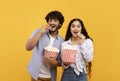 Excited indian man and woman eating popcorn at cinema, standing over yellow studio background Royalty Free Stock Photo