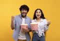 Excited indian man and woman eating popcorn, watching movie or football game, celebrating success of their team Royalty Free Stock Photo