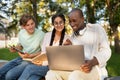 Excited international students studying in park, enjoying the results of their job, looking at laptop screen Royalty Free Stock Photo