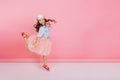 Excited joyful amazing girl with long brunette hair, in princess mask on head jumping in tulle skirt on pink