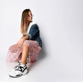 Young teen girl model in stylish casual clothes and sneakers sitting and looking away camera over white background