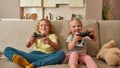 Excited kids, little boy and girl playing video games using joystick or controller while sitting together on sofa at Royalty Free Stock Photo