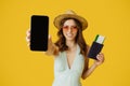 Excited lady going vacation, showingcellphoen with blank screen and passport with flight tickets, mockup