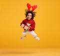 Excited little african american boy in Christmas sweater and deer antlers jumping up in air with Xmas gift box Royalty Free Stock Photo