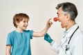 Excited little boy touching clown nose of friendly male pediatrician, isolated over grey background. Doctor and little Royalty Free Stock Photo