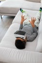 Excited little kid using virtual reality glasses. He lying on gray sofa and using new gadget technology Royalty Free Stock Photo