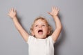 Excited little toddler girl baby in white T-shirt isolated over gray background raised hear arms having fun alone screaming with Royalty Free Stock Photo